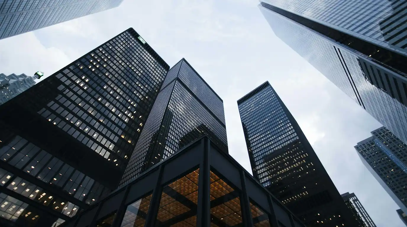 Black glass towers seen from below above a lit glass pavilion