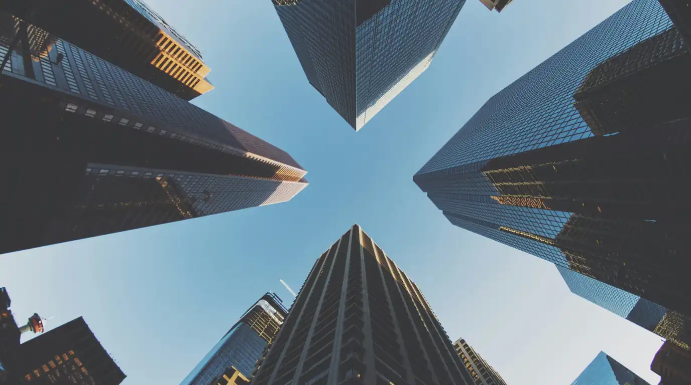 Office towers radiating outward against a clear blue sky, seen from street level looking up.