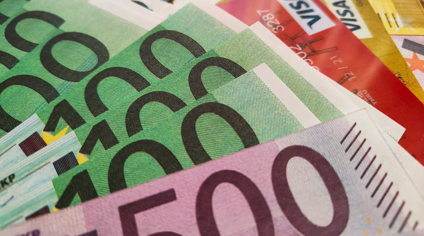 Fanned green and pink banknotes overlapping a red and a gold payment card in a tight, close-cropped view.