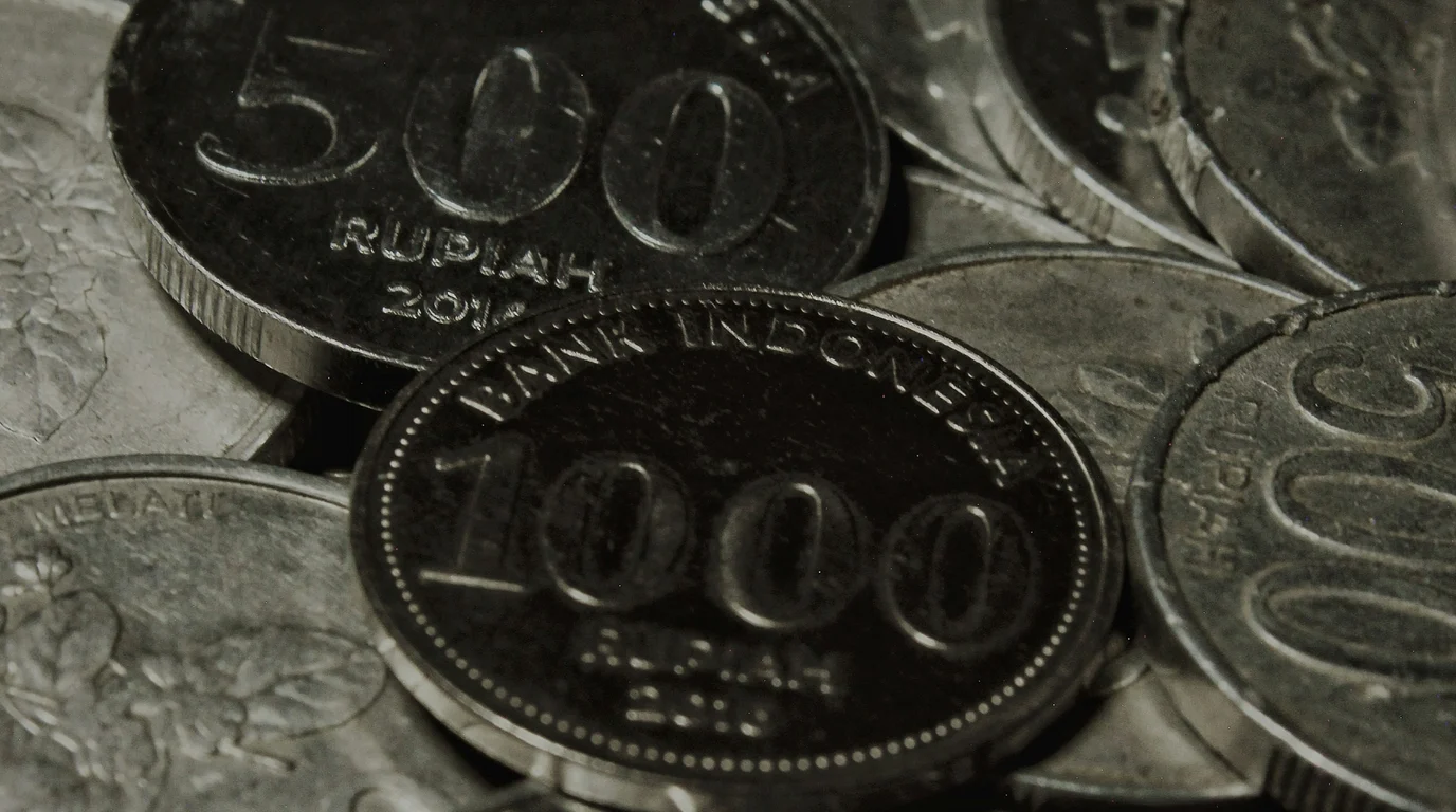 A near-monochrome close-up of milled coins piled together, the largest stamped with a beaded rim and the numeral 1000.