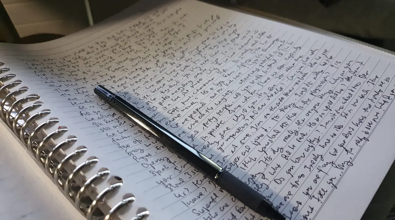 An open spiral notebook filled with handwritten notes, a black pen lying across the page.