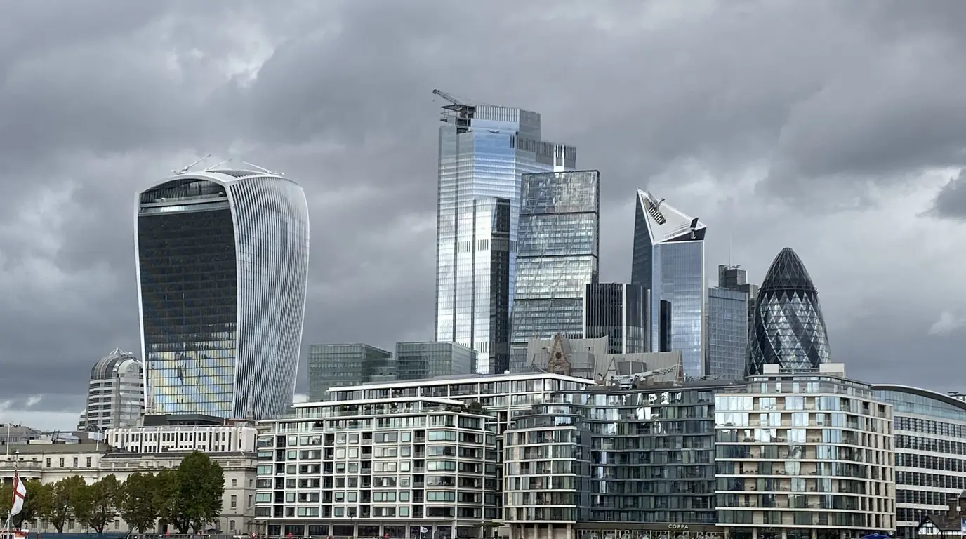The City of London skyline under grey cloud, seen across the River Thames.